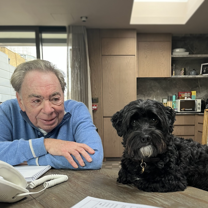andrew lloyd webber leans on a table with a black dog with a white beard
