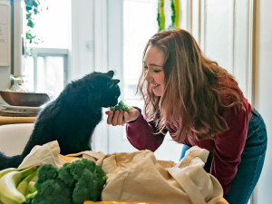 Woman offering broccoli to her black cat.
