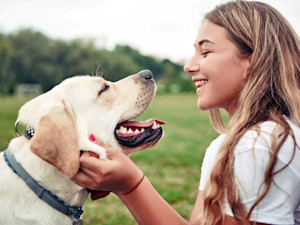 Woman smiling at her Lab dog outside in the grass.