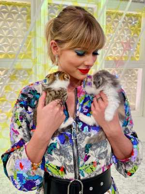 Taylor Swift holding two small kittens in each hand and smiling down at them