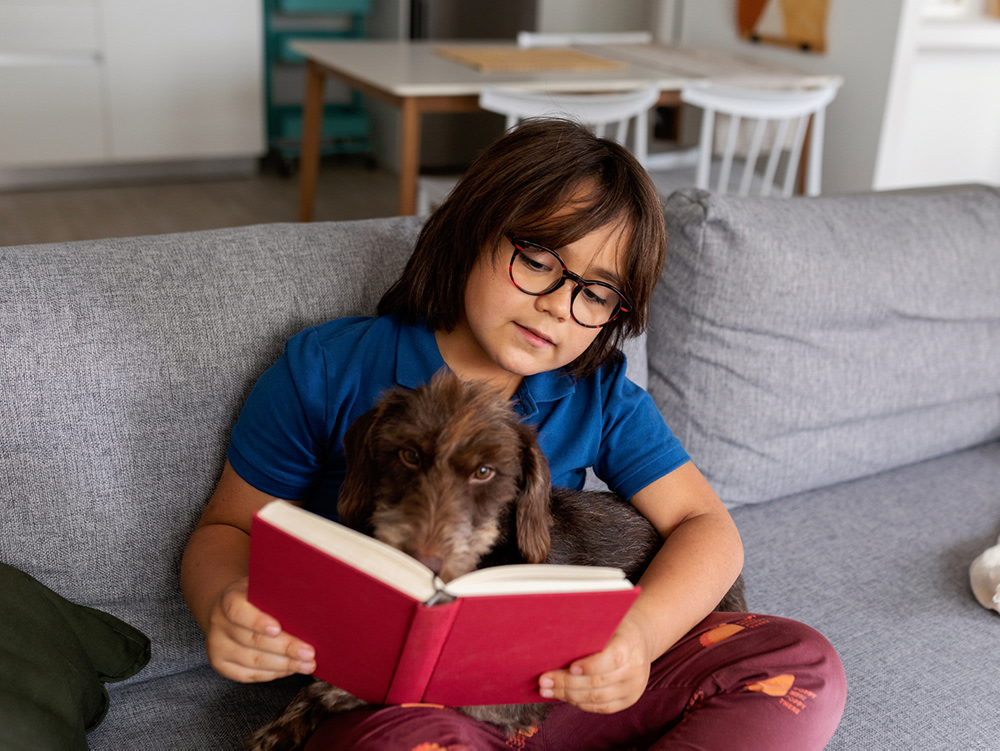 Boy reading a book on the sofa to his dog