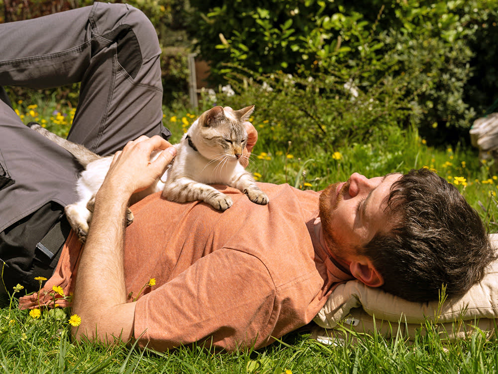 Man laying with his cat on his stomach outside.