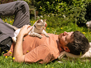 Man laying with his cat on his stomach outside.