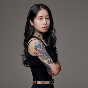 A studio portrait of a tattooed woman posing with her arms crossed. 