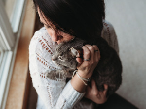 Woman in a white sweater hugging her cat next to a window