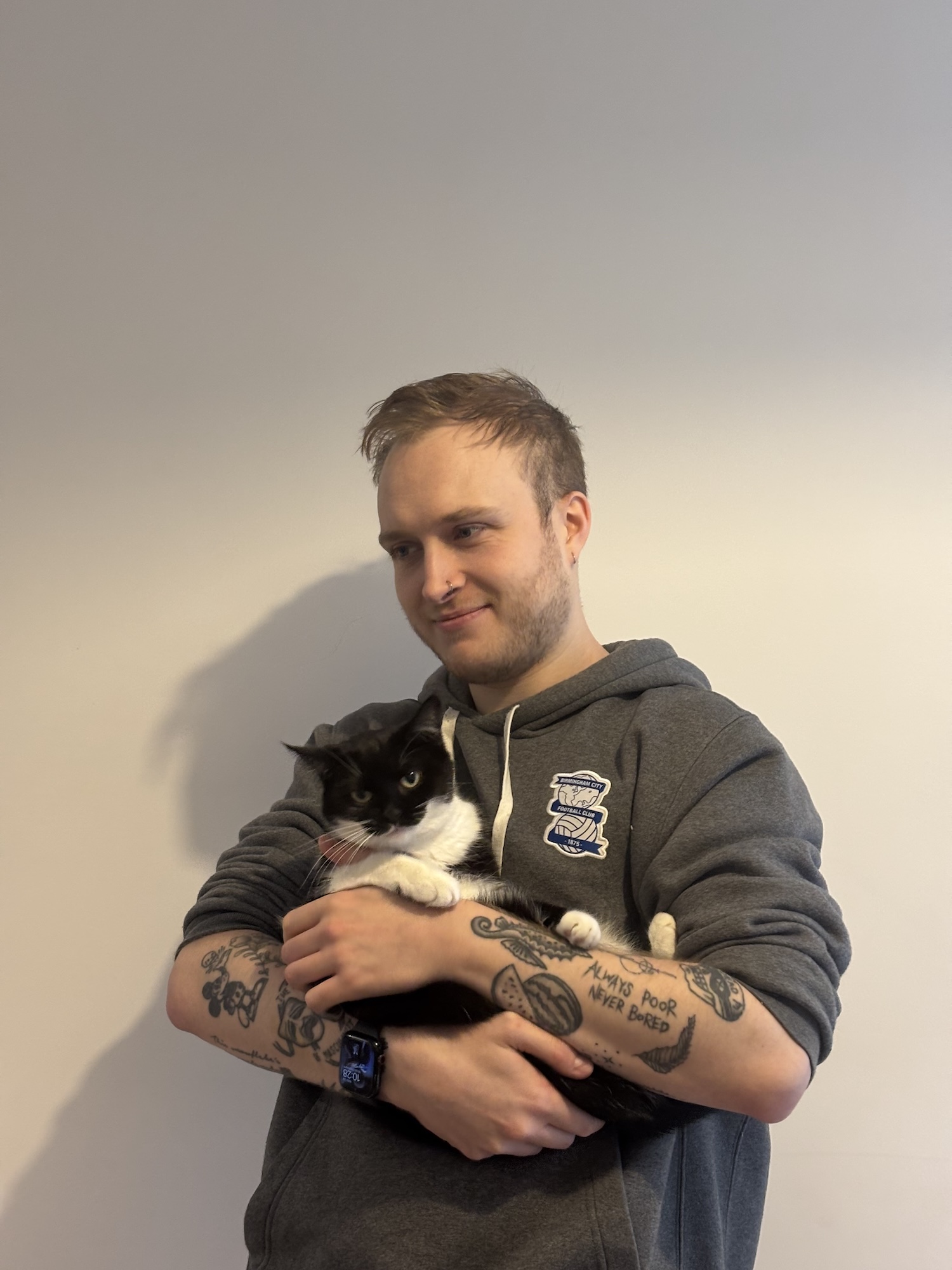 a picture of a man wearing a hoodie with tattoos holding a black and white cat