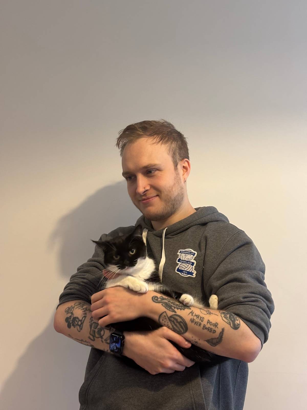 a picture of a man wearing a hoodie with tattoos holding a black and white cat