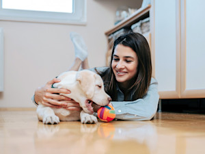 woman lying on floor hugging lab puppy playing with ball