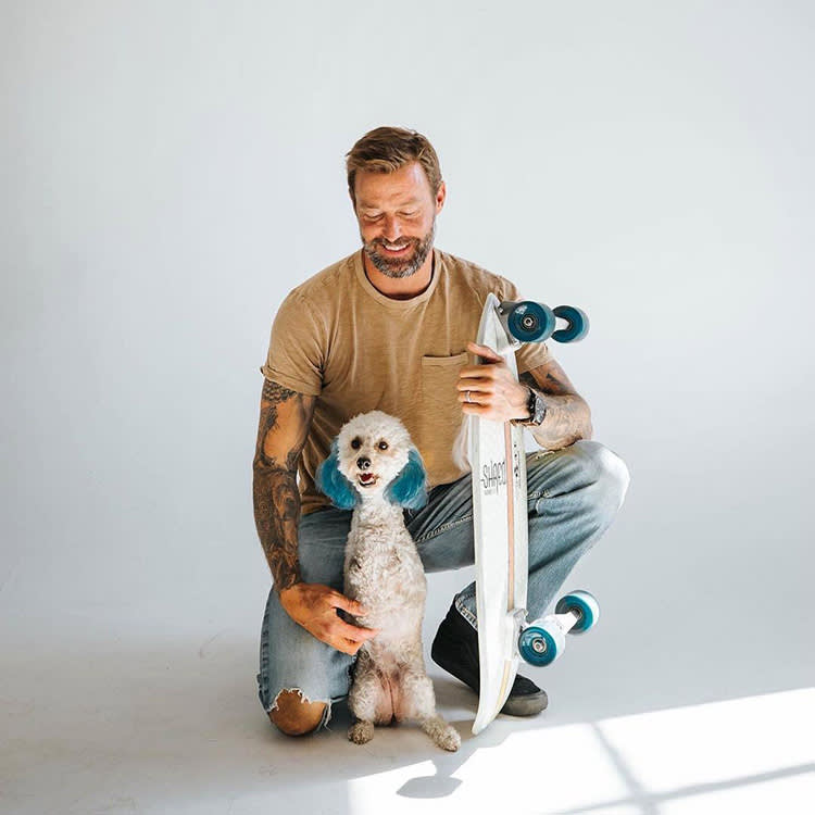 Zach Skow posing with a dog and a skateboard. 