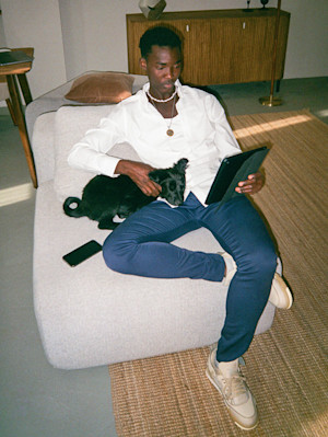 a cool man sits in a minimalist chair reading an ipad with a small black dog