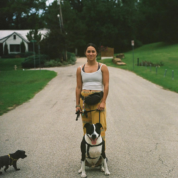 Brit Hensel standing behind her dog on a leash on a rock path outside in front of a house