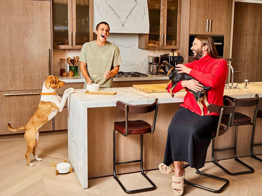 Co-owners, Antoni and JVN of yummers pets in the kitchen laughing with two dogs. 