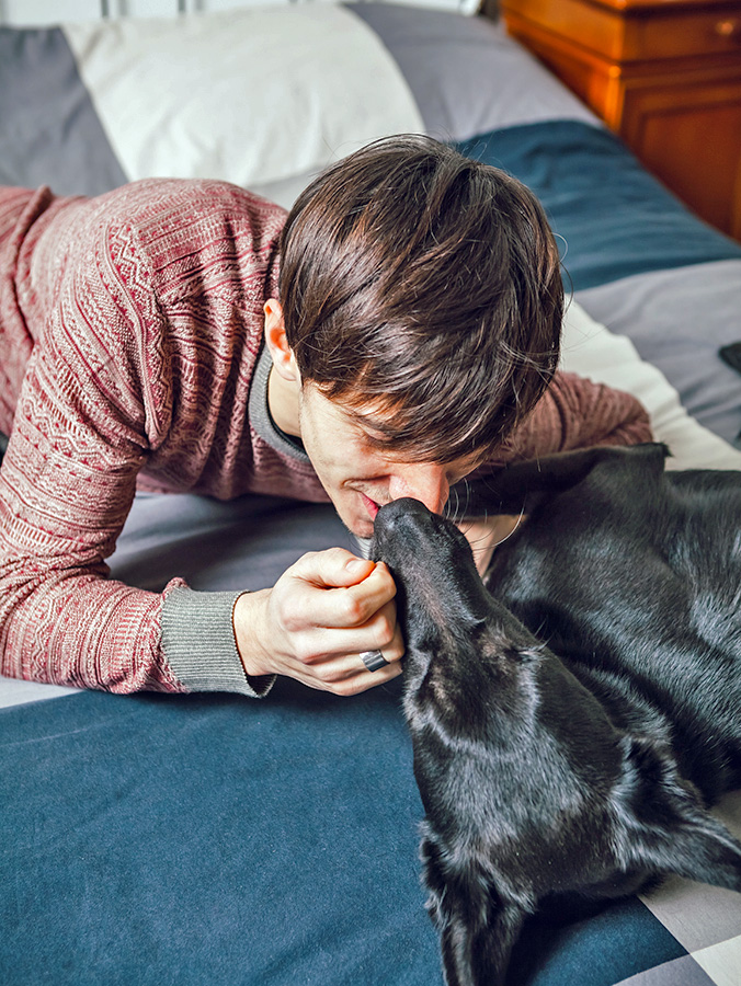 Man snuggling dog's face at home in bed.