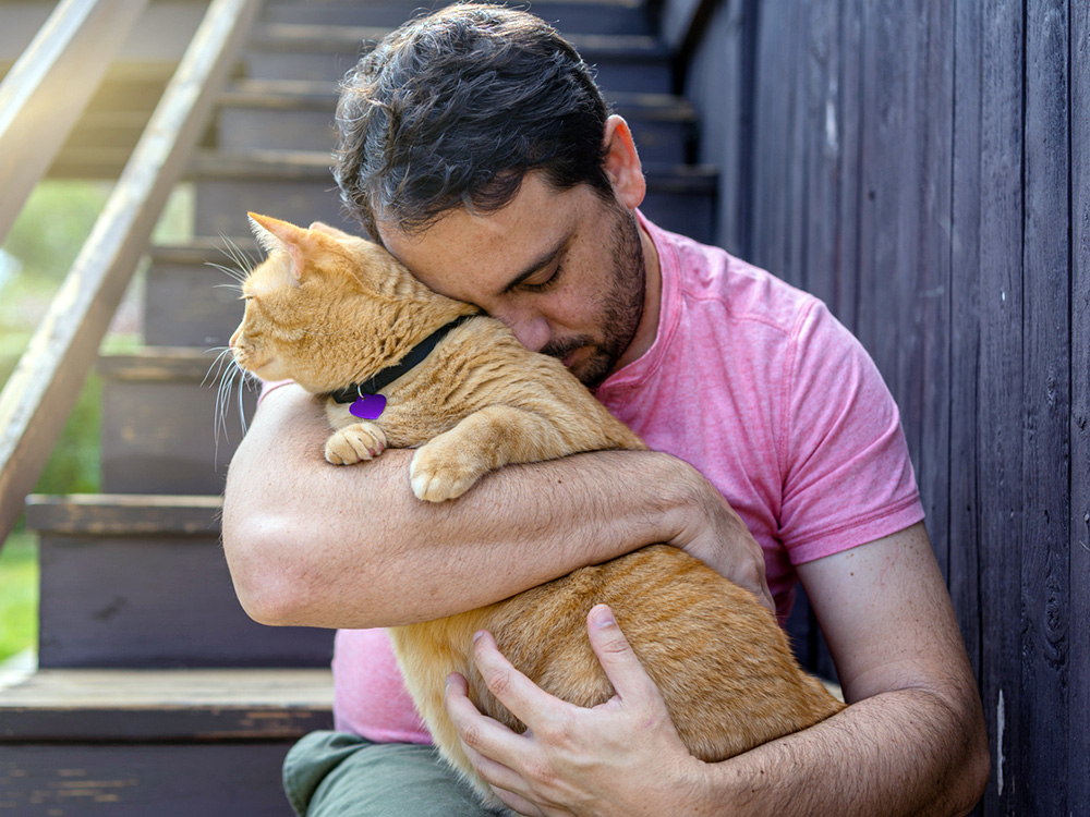 Man holding his orange cat in his arms outside.