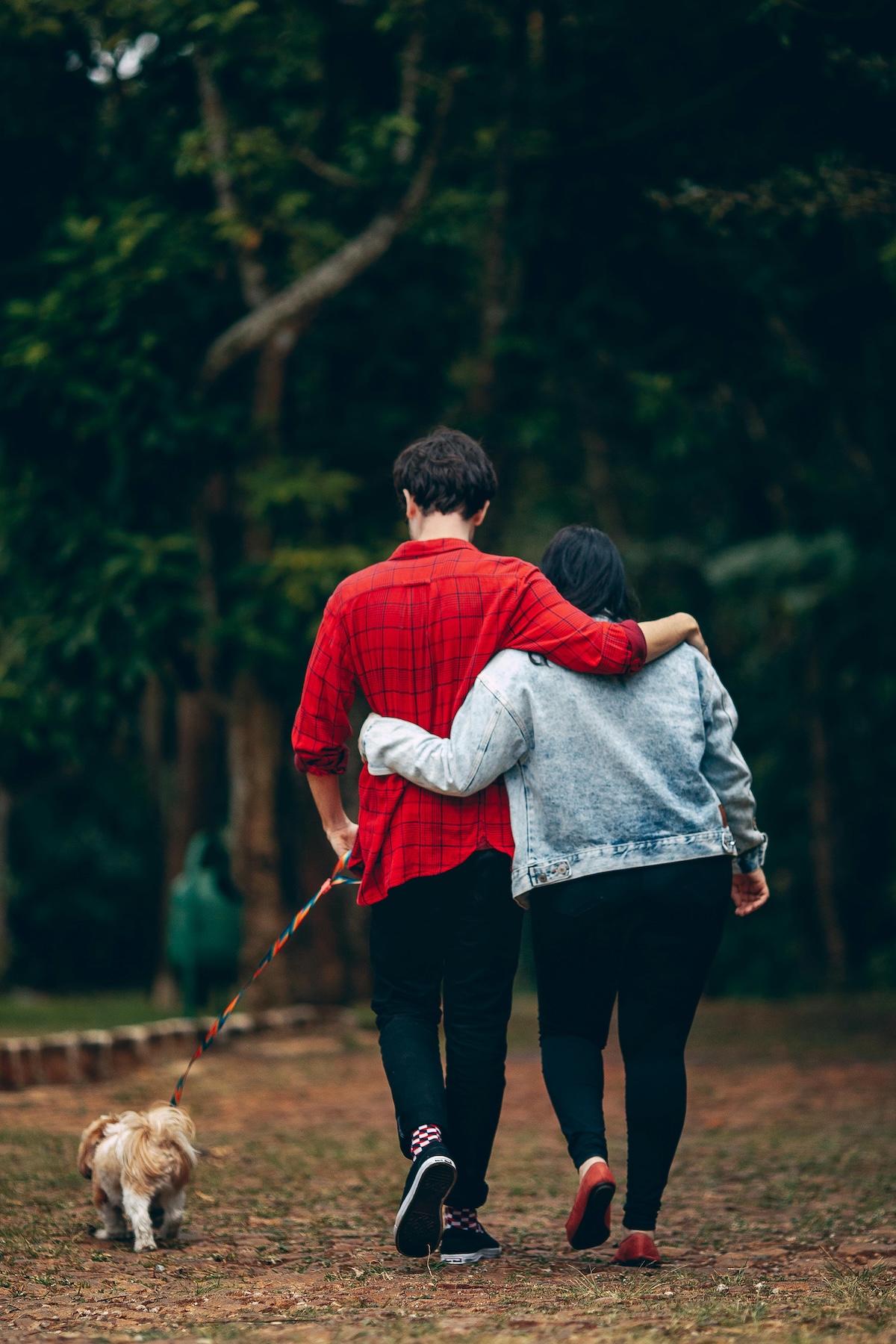 a picture of a couple walking in the woods with their dog on the leash
