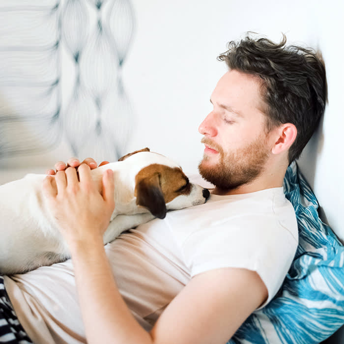 Man holding his small white dog in bed.
