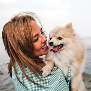 Woman snuggling her small dog outside.