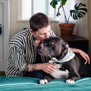 Woman kisses her black pit bull dog on the head.