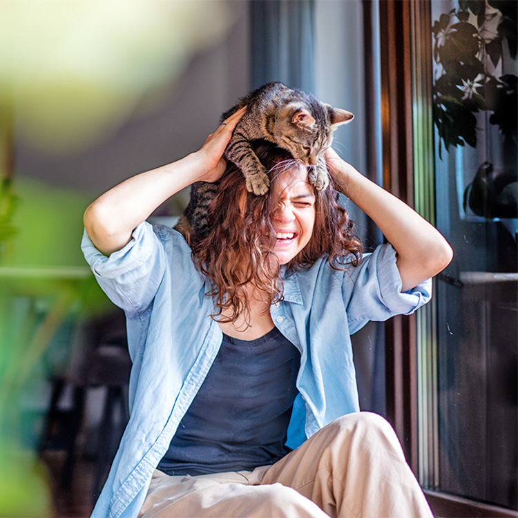 Woman laughing while her cat climbs on her head.