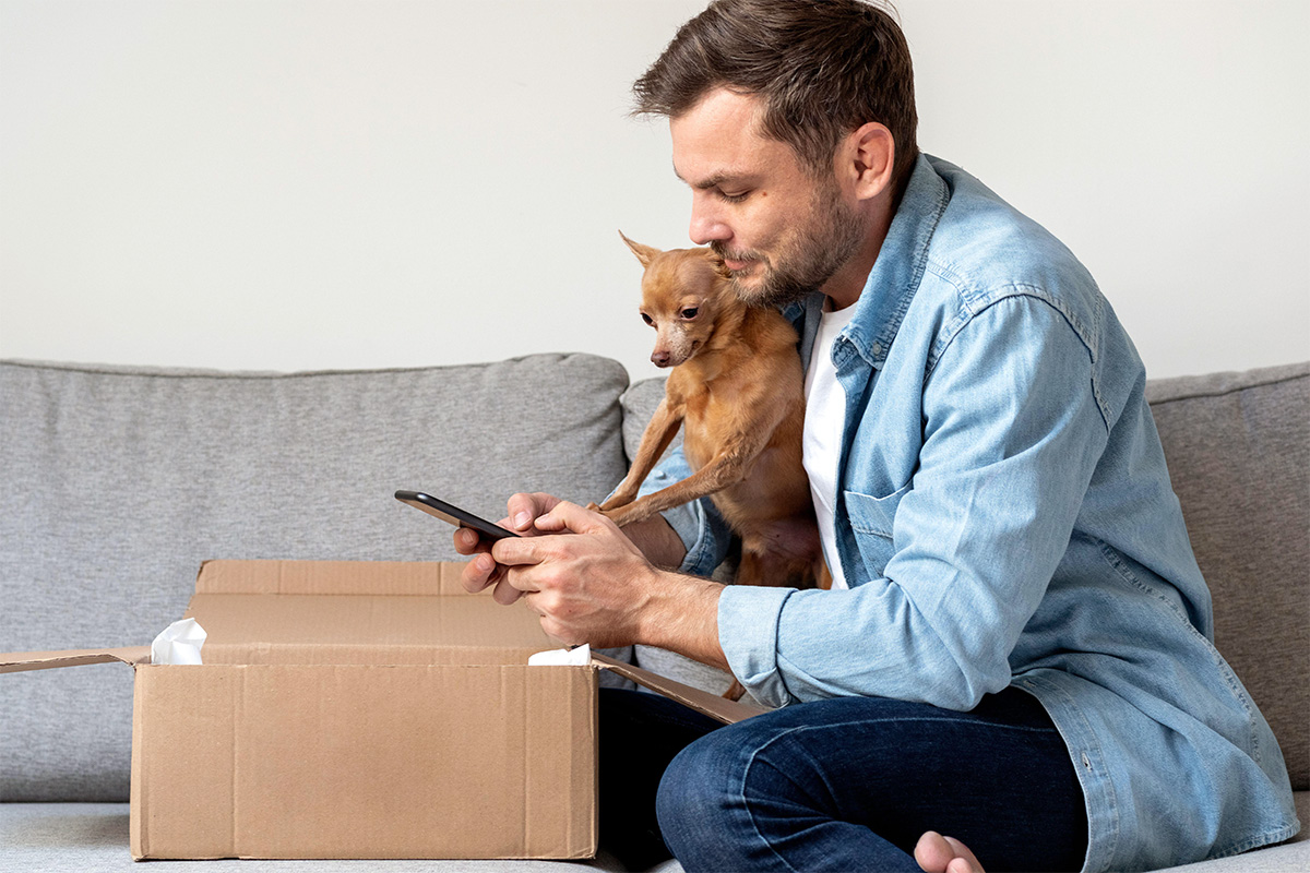 man holding phone and dog while receiving a package