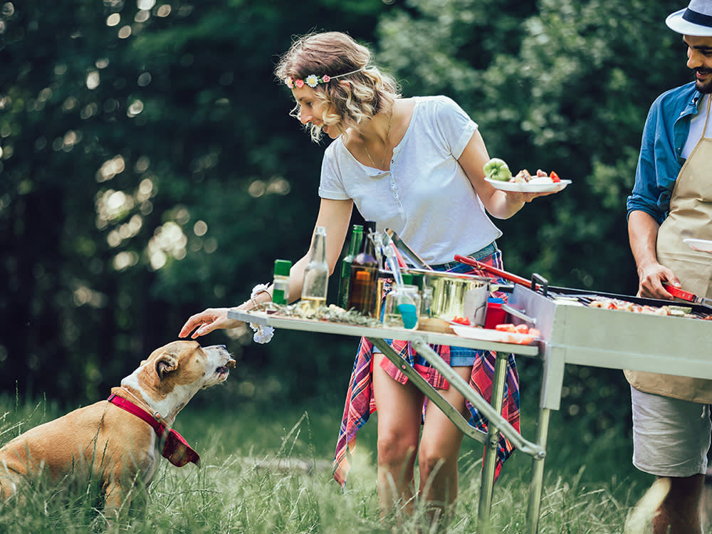 A woman and a man grilling outside with a dog. 