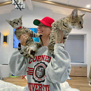 hailey bieber wears a red hat and holds two savannah cats