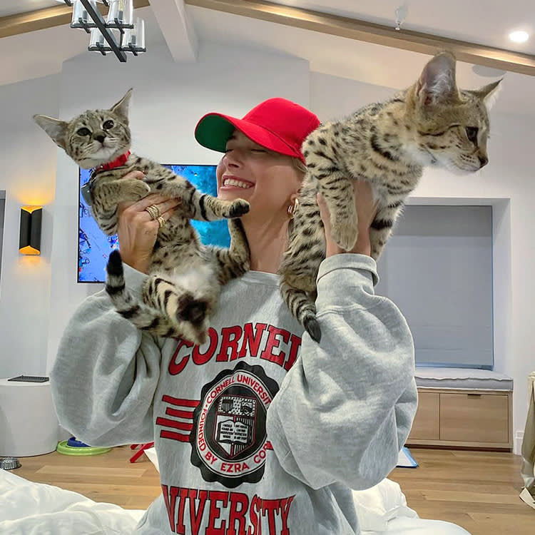 hailey bieber wears a red hat and holds two savannah cats