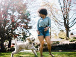 A woman with curly black hair playing with her white labradoodle dog outside