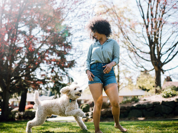 A woman with curly black hair playing with her white labradoodle dog outside