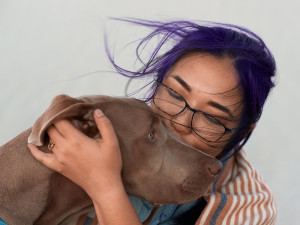 Woman with purple hair kissing the face of her chocolate brown hound dog 