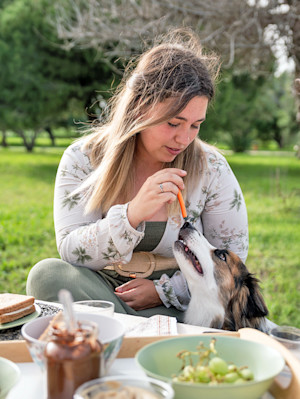 Woman feeding her dog a carrot outside.