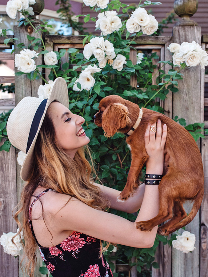 A woman in her twenties walking her puppy down the street in the summer time.