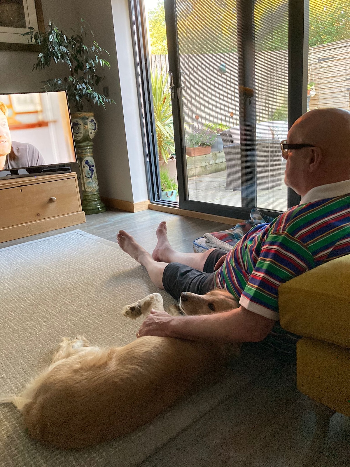 a picture of an older man sitting on the floor cuddling a golden dog and watching TV