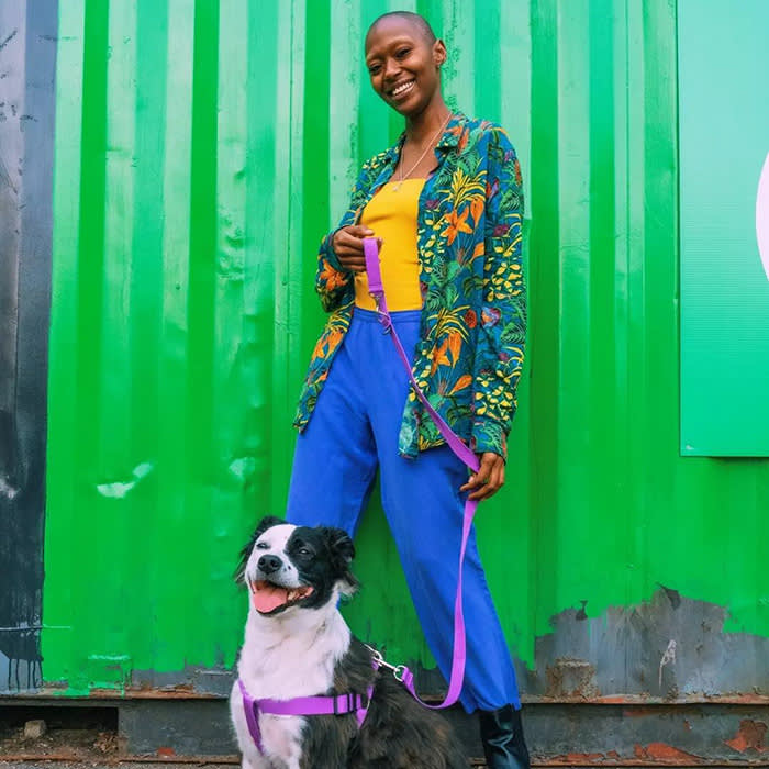 model standing in front of green wall holding lavender leash attached to dog