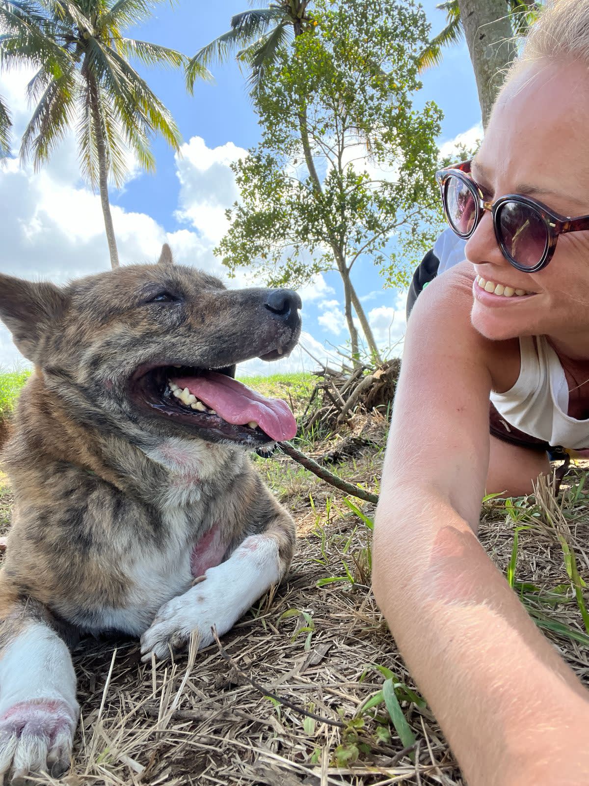 a blonde woman wearing sunglasses smiles at a dog