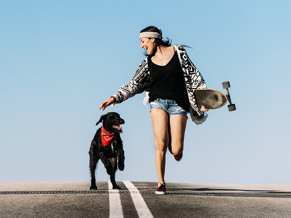 Woman with a skateboard running with her dog 