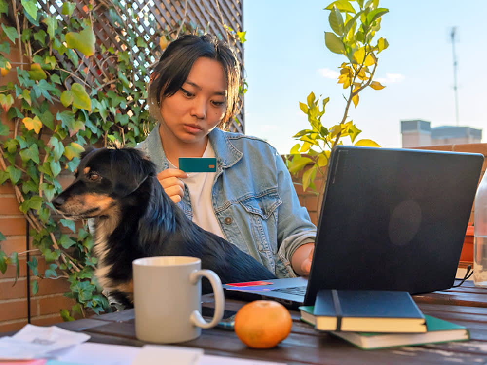 a picture of a woman looking at a laptop and a bank card with a small dog on her lap