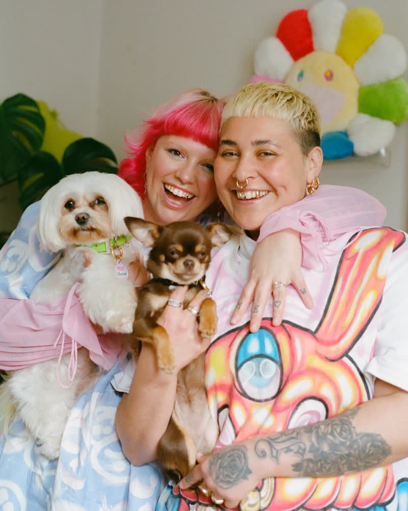 two women in bright clothes with bright hair hold two little dogs