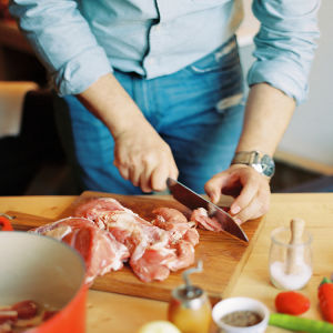 A man cutting raw chicken on a cutting board in the kitchen