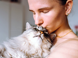 Woman cuddling her pet cat at home.