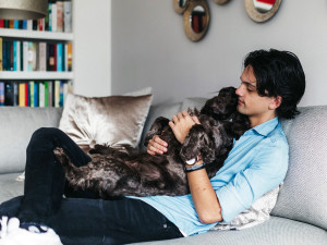 Young Man Cuddling Cocker Spaniel Dog On His Lap On The Couch At Home.

