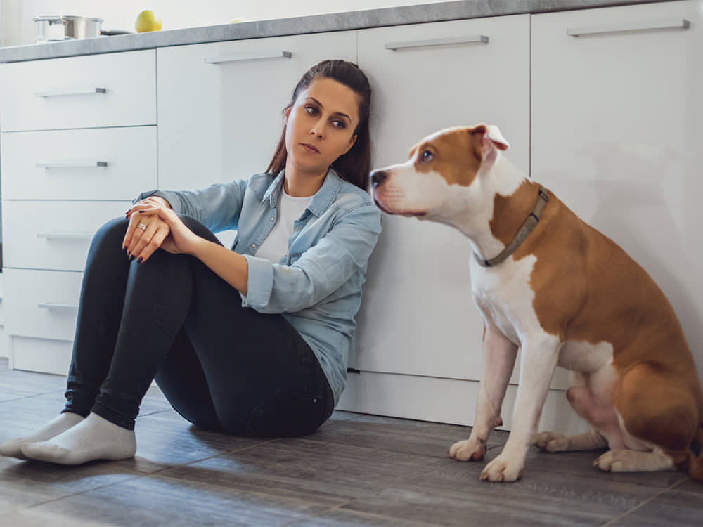 Sad woman sitting on a kitchen floor and looking at her dog.
