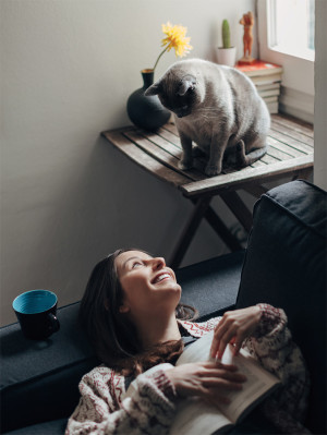 Woman With A Book And Her Cute Cat At Home.
