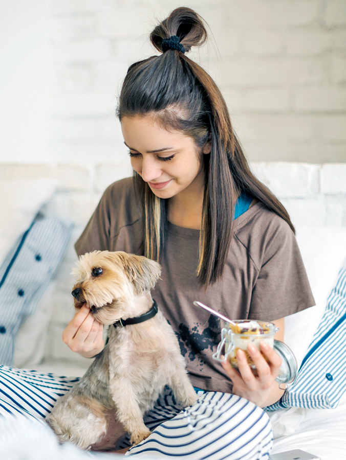 Woman feeding her small dog some yogurt.