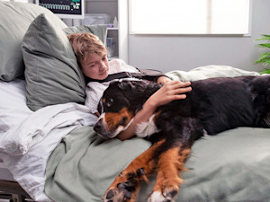 Sick child resting in hospital bed, cuddling therapy dog.