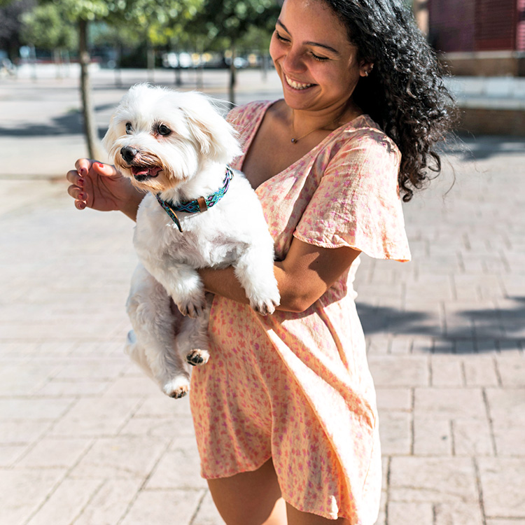 Woman holding her white dog outside.