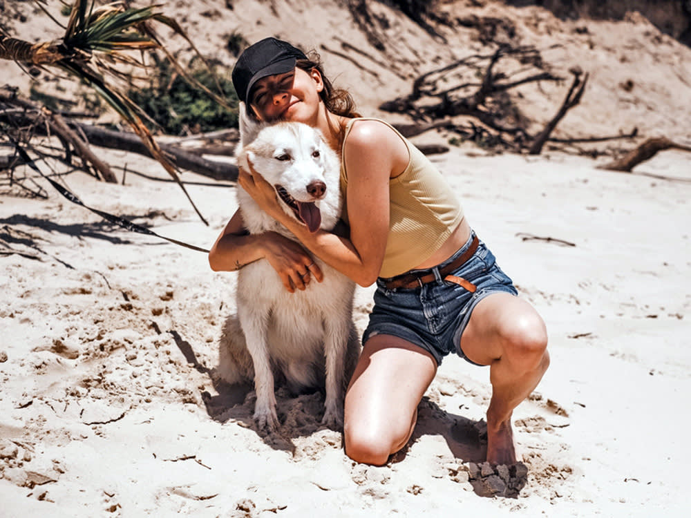 girl in a yellow top and baseball cap hugs a big fluffy white dog on a beach