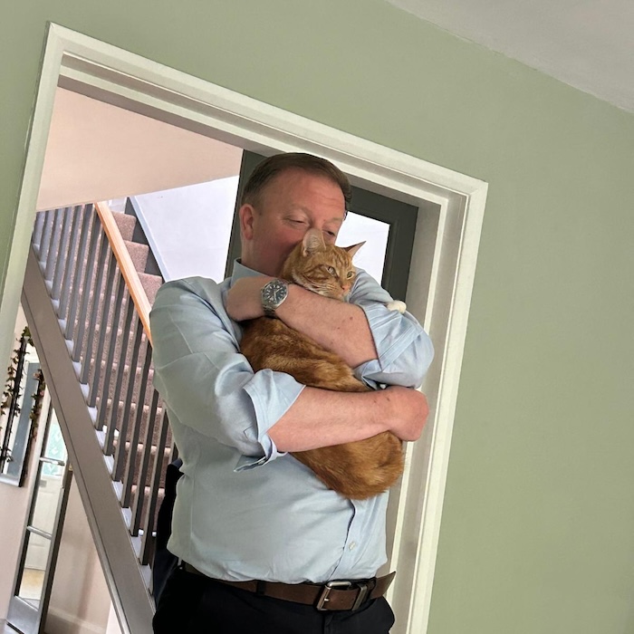 a man hugs a ginger cat very close