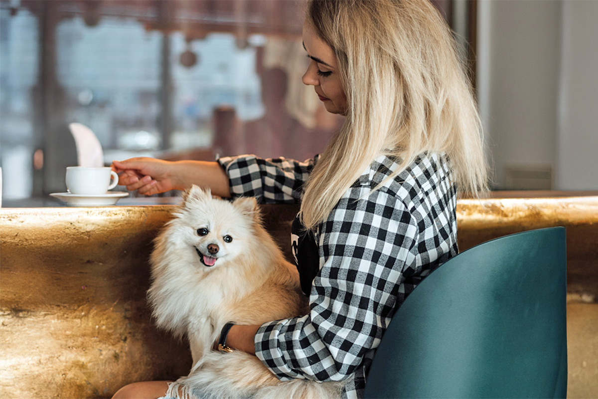 a white blonde woman holds a Pomeranian while she sips coffee at a cafe