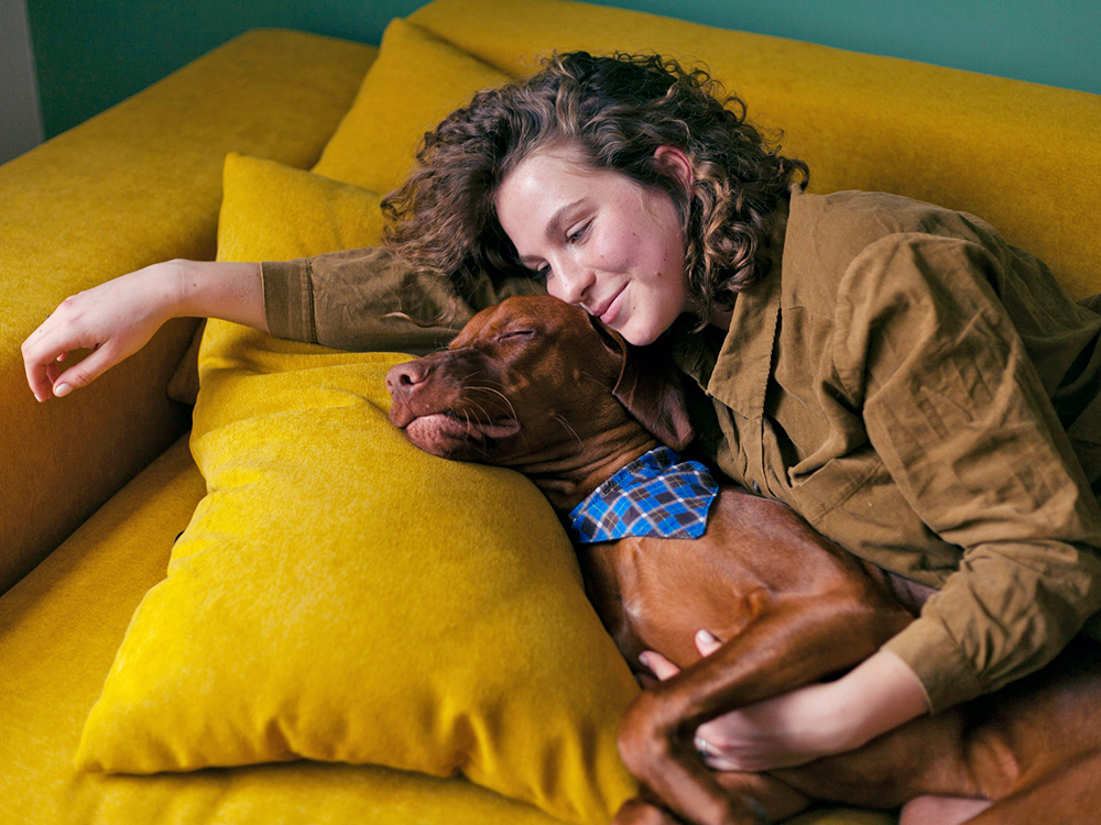 Woman snuggling her dog on the couch at home.